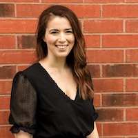 A headshot of writer Laura Hanrahan standing in front of a red brick wall and wearing a black blouse.