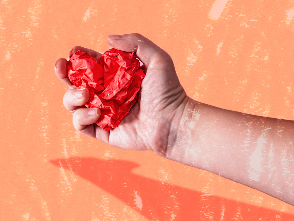 Someone crushing a heart with their hand because of emotional cheating